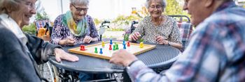 Senioren spielen draußen auf der Terrasse gemeinsam Mensch ärger dich nicht