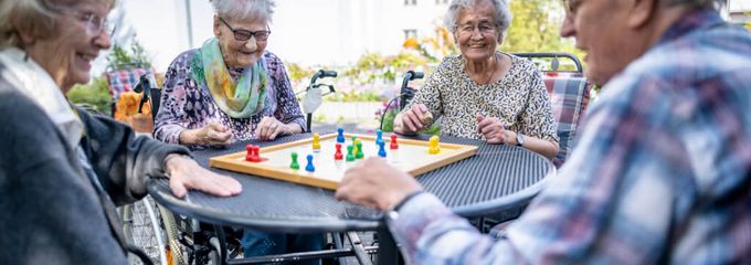 Senioren spielen draußen auf der Terrasse gemeinsam Mensch ärger dich nicht