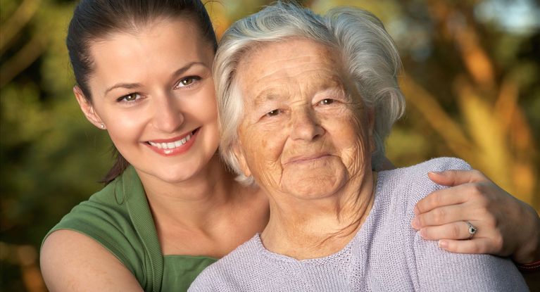 Junge lächelnde Frau fasst Senioren an der Schulter