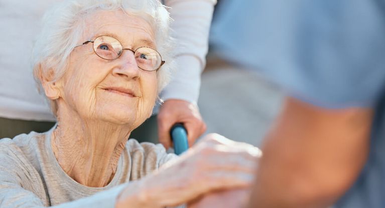 Pflegerin hält Hand einer Seniorin im Rollstuhl