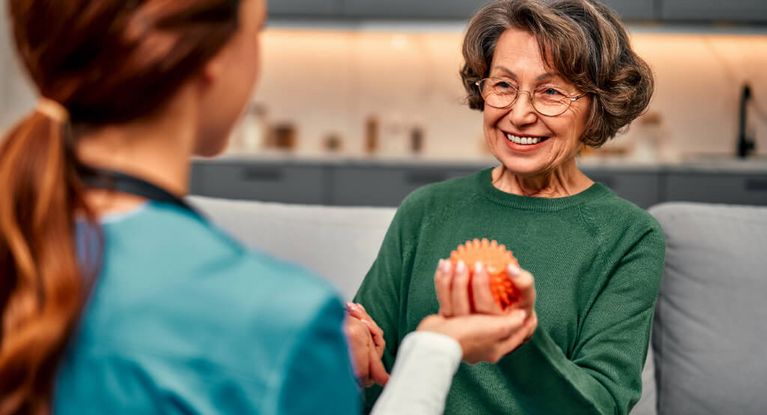 Pflegerin und Seniorin halten einen roten Massageigel