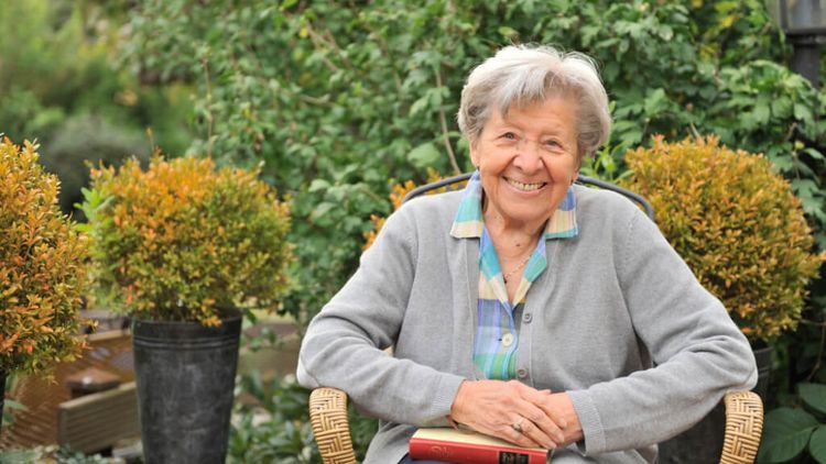 freundliche ältere Frau sitzt im Garten auf einem Stuhl