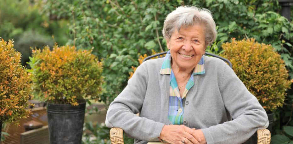 freundliche ältere Frau sitzt im Garten auf einem Stuhl
