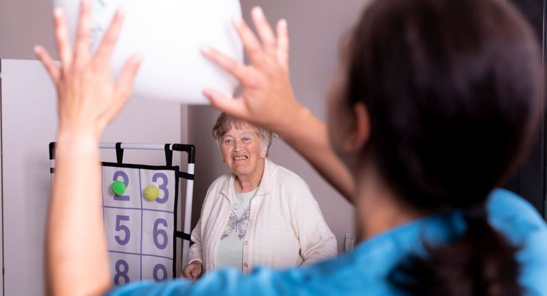 Pflegerin spielt mit Altenheimbewohnerin und einem Kissen