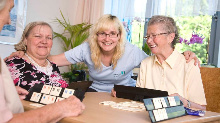 Altenpflegerin und Seniorinnen spielen gemeinsam Rummy
