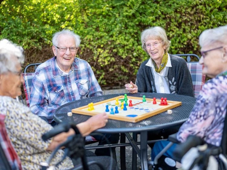 Fröhliche Senioren spielen Mensch-Ärger-Dich-Nicht draußen im Garten