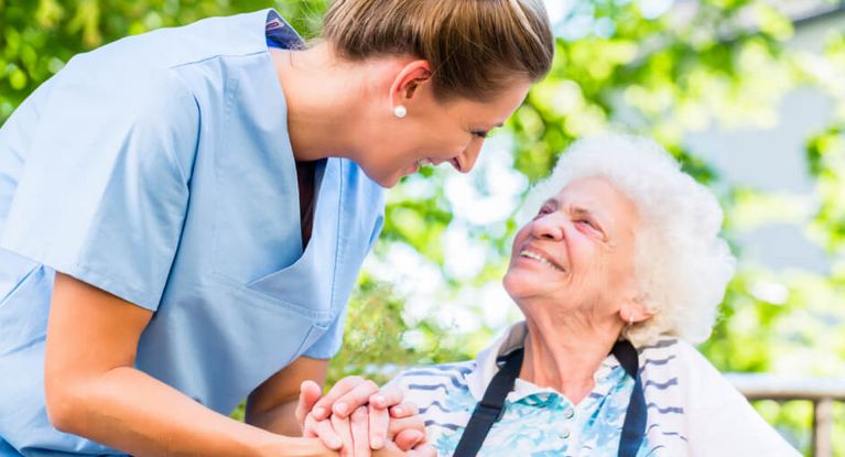 Altenpflegerin hält die Hand einer lächelnden Seniorin im Rollstuhl