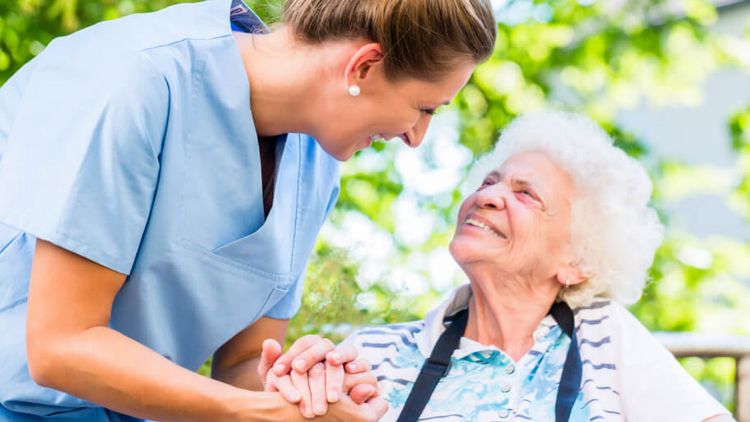 Altenpflegerin hält die Hand einer lächelnden Seniorin im Rollstuhl